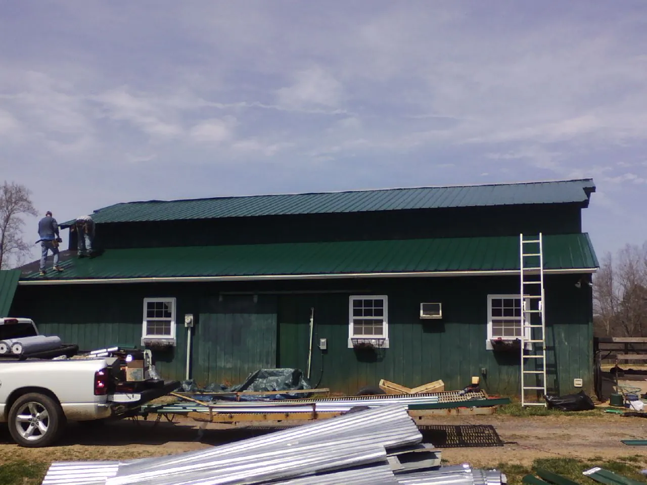 Crew installing green metal roofing on a large green barn in Lisbon
